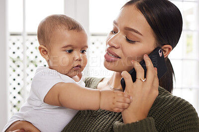 Buy stock photo Shot of a young woman using a smartphone while carrying her baby at home