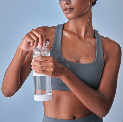 Buy stock photo Studio shot of a fit young woman drinking bottled water against a grey background
