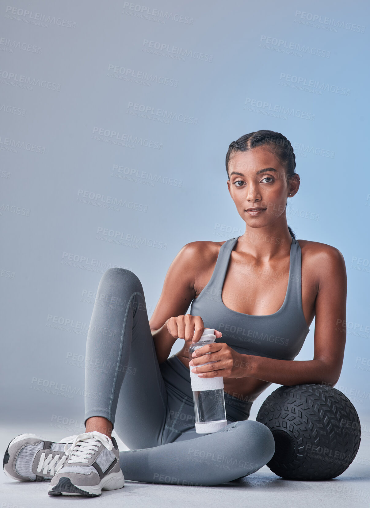 Buy stock photo Studio shot of a fit young woman drinking bottled water against a grey background