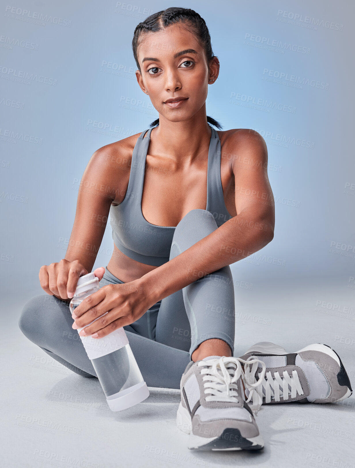 Buy stock photo Studio shot of a fit young woman drinking bottled water against a grey background