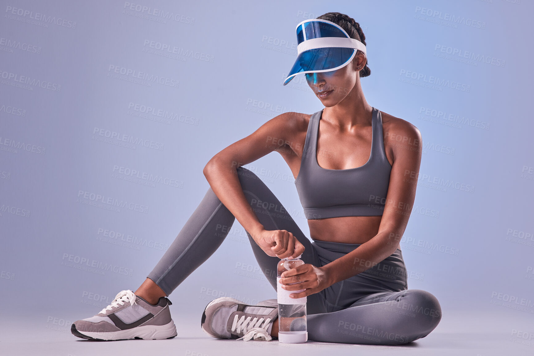 Buy stock photo Studio shot of a fit young woman drinking bottled water against a grey background