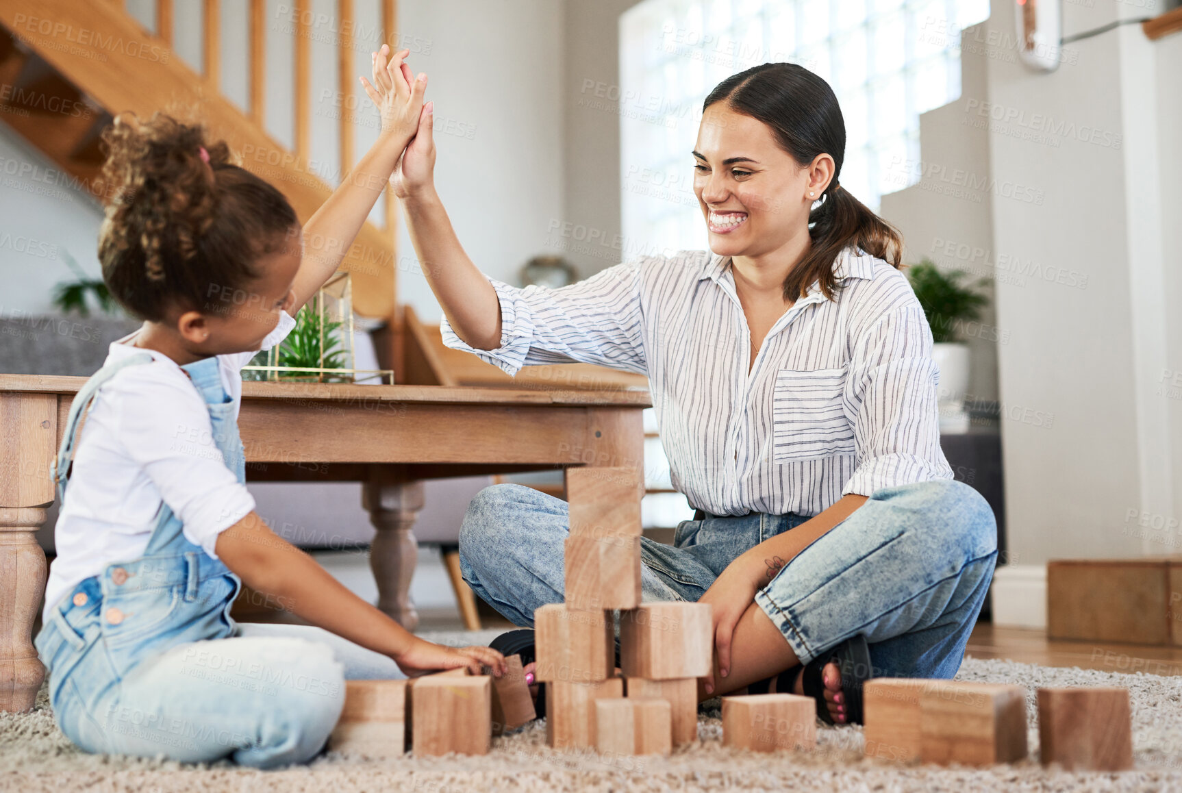 Buy stock photo Shot of a mother and her daughter giving each other a high five while playing with wooden blocks together at home