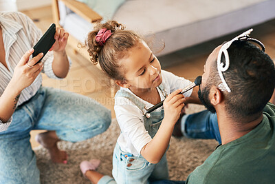 Buy stock photo Shot of a little girl putting makeup on her father while her mother takes pictures of them at home