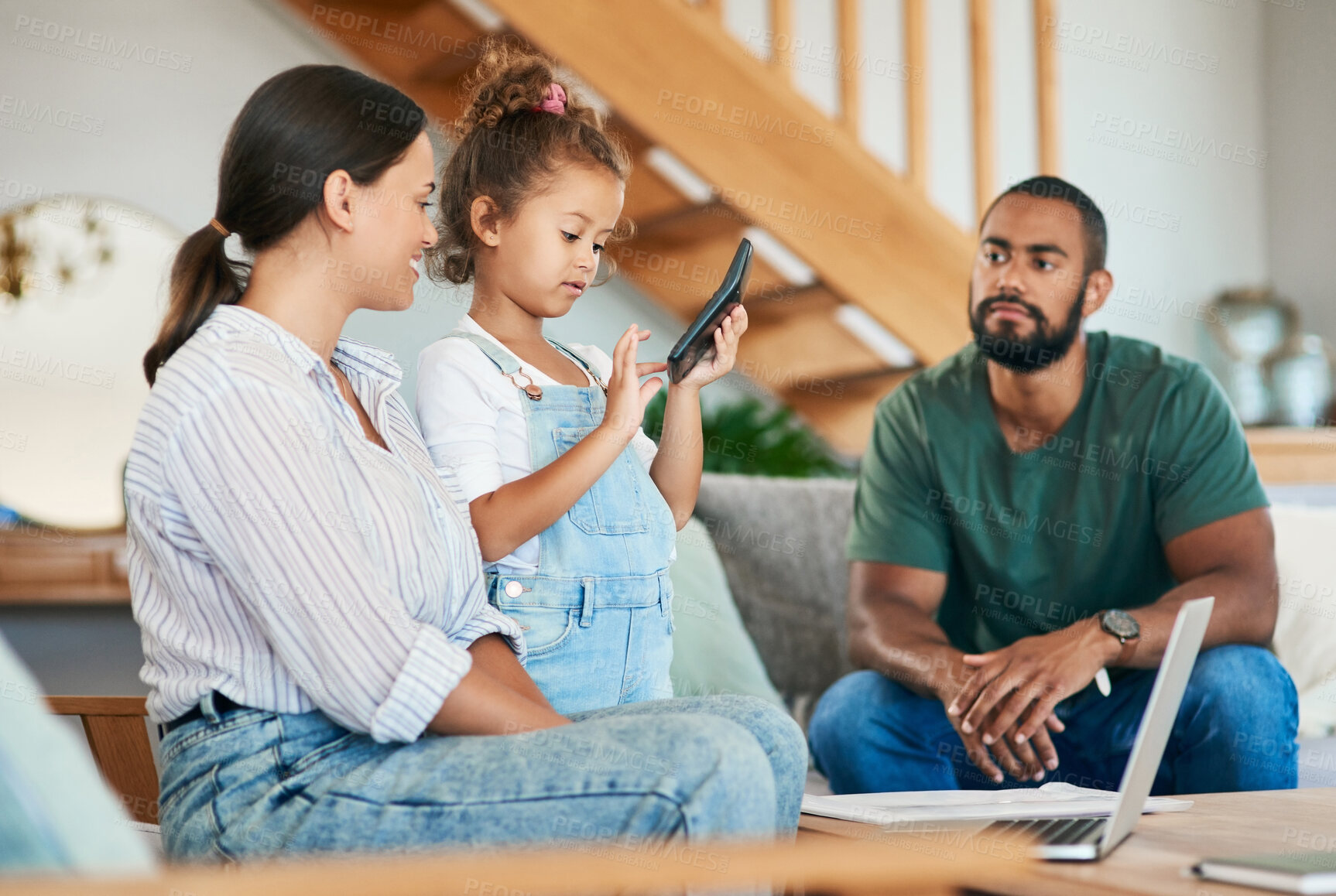 Buy stock photo Shot of an adorable little girl using a calculator while her parents are working on their budget at home