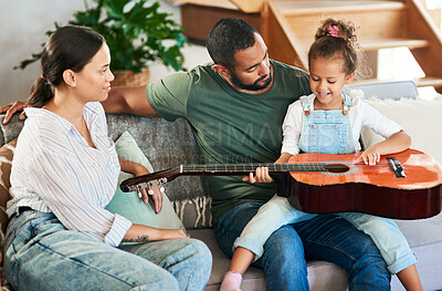 Buy stock photo Shot of an adorable little girl playing an acoustic guitar while relaxing with her parents at home