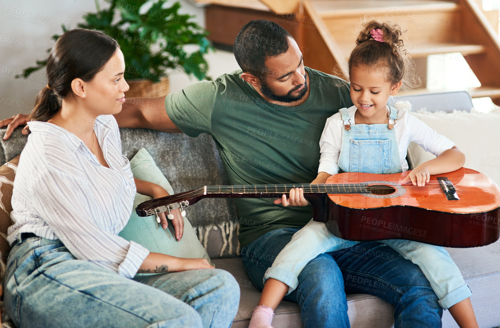 Buy stock photo Shot of an adorable little girl playing an acoustic guitar while relaxing with her parents at home