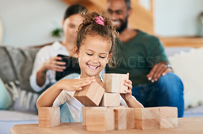 Buy stock photo Shot of an adorable little girl playing with wooden blocks while her parents are relaxing in the background at home