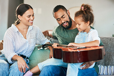 Buy stock photo Shot of an adorable little girl playing an acoustic guitar while relaxing with her parents at home