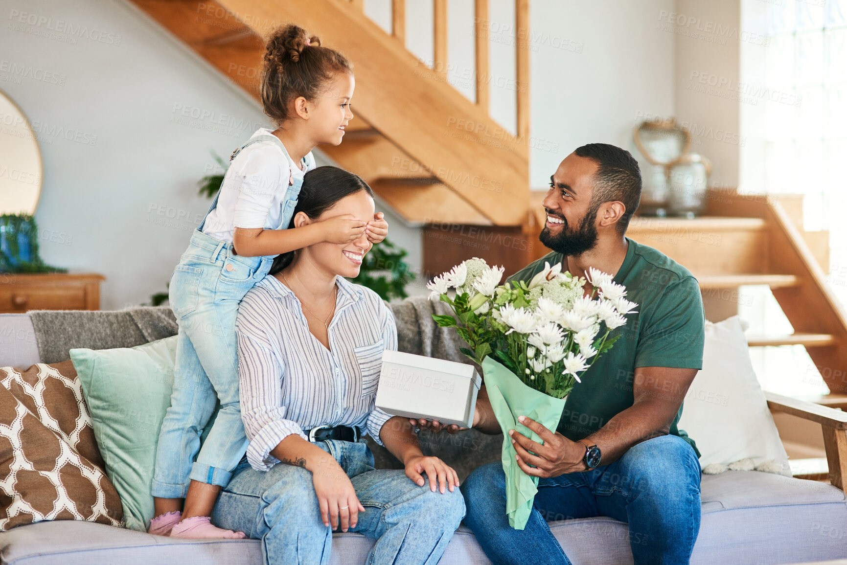 Buy stock photo Shot of a woman getting a gift and bouquet of flowers from her husband and little daughter at home