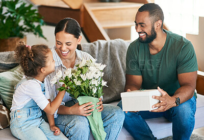 Buy stock photo Shot of a woman getting a gift and bouquet of flowers from her husband and little daughter at home