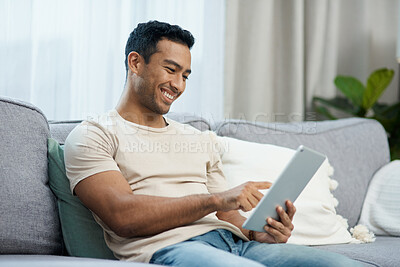 Buy stock photo Tablet, smile and relax with a man on a sofa in the living room of his home for social media browsing. Technology, app or gaming search with a happy young person in his apartment on the weekend