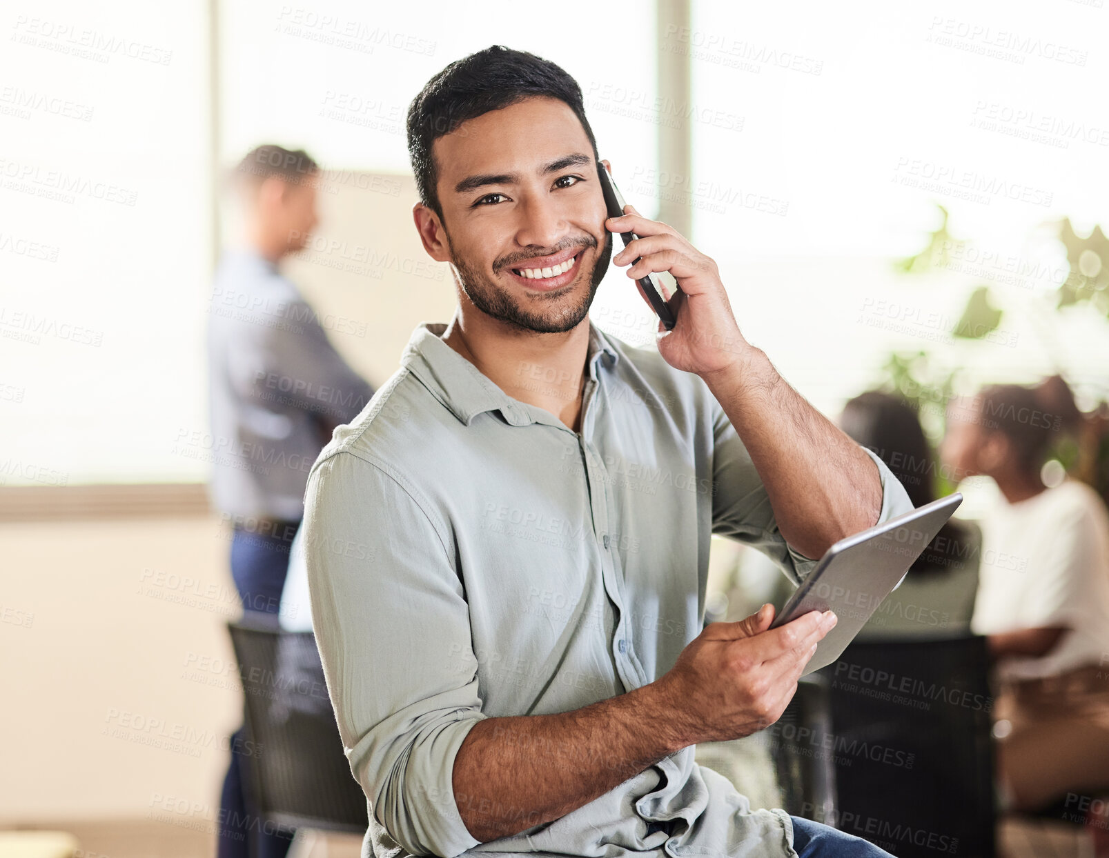 Buy stock photo Shot of a young businessman using his smartphone to make a phone call while holding his digital tablet