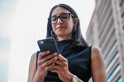 Buy stock photo Low angle shot of an attractive young businesswoman sending a text while standing outside on the office balcony