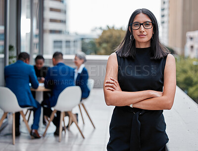 Buy stock photo Cropped portrait of an attractive young businesswoman standing with her arms folded outside on the office balcony with her colleagues in the background