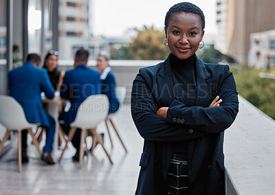 Buy stock photo Cropped portrait of an attractive young businesswoman standing with her arms folded outside on the office balcony with her colleagues in the background