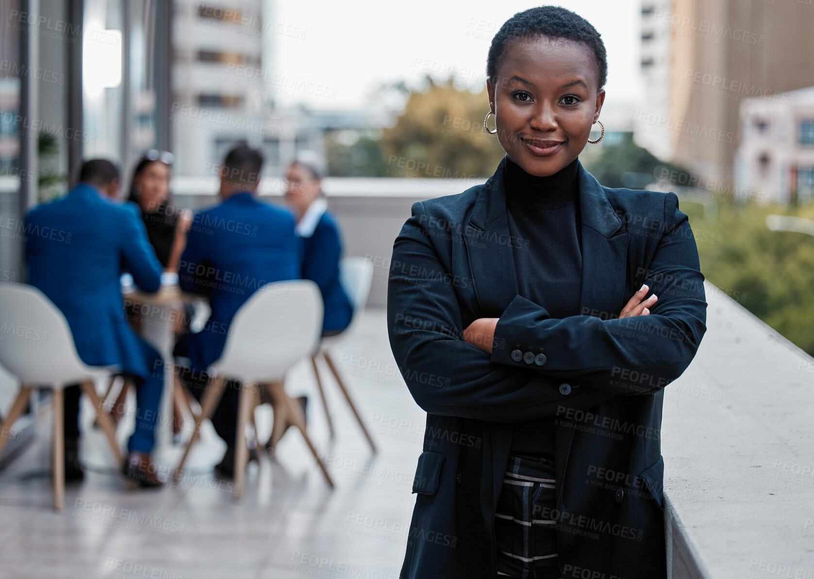 Buy stock photo Cropped portrait of an attractive young businesswoman standing with her arms folded outside on the office balcony with her colleagues in the background