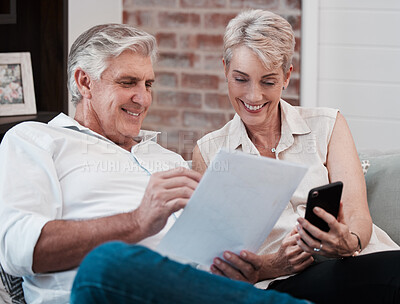 Buy stock photo Shot of a mature couple looking at paperwork while using a cellphone on the sofa at home