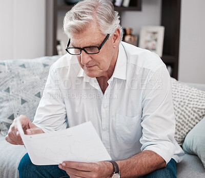 Buy stock photo Shot of a mature man checking some paperwork on the sofa at home