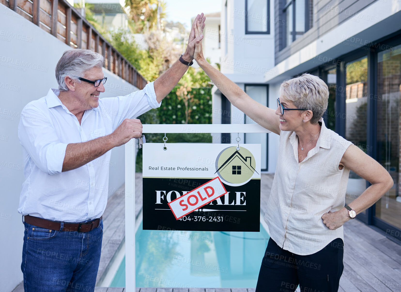 Buy stock photo Cropped shot of two mature people high fiving while standing in front of a for sale board with a sold sticker on it