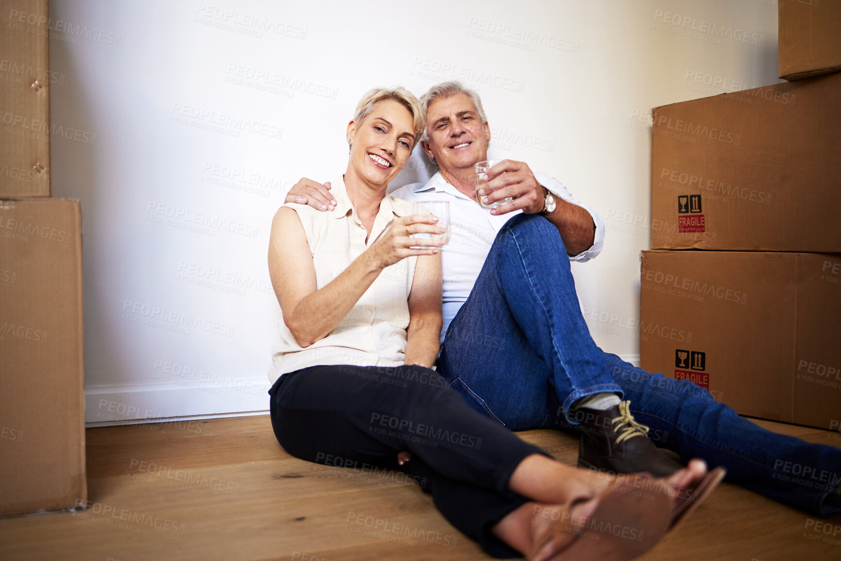 Buy stock photo Shot of a mature couple toasting with water after a successful day moving house