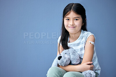 Buy stock photo Plaster, portrait and girl child with teddy bear for comfort in studio isolated on blue background. Happy, hug and vaccine with young kid embracing stuffed animal toy for healthcare or medical