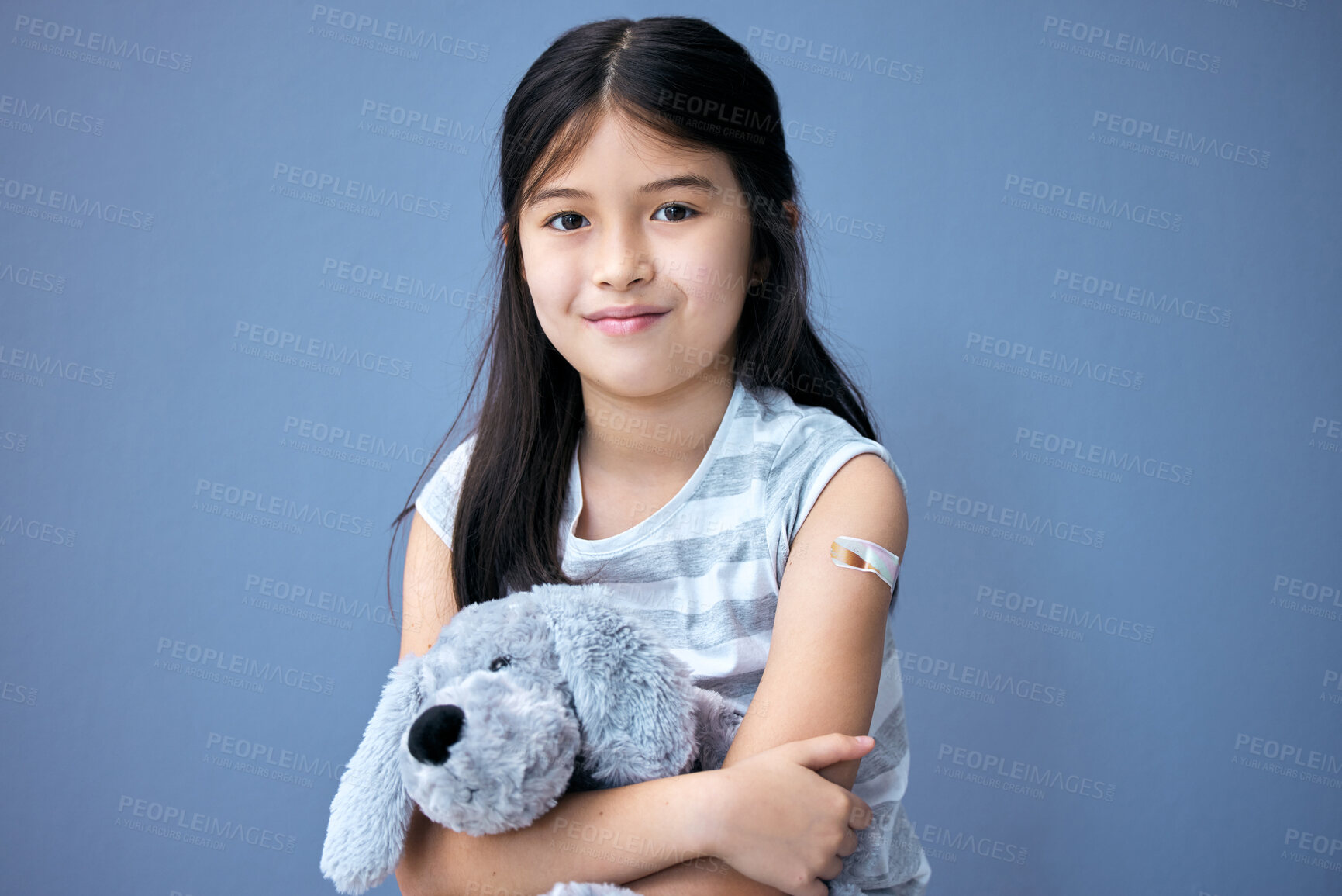 Buy stock photo Shot of an adorable little girl sitting in the studio after getting her Covid vaccine and holding a teddy bear