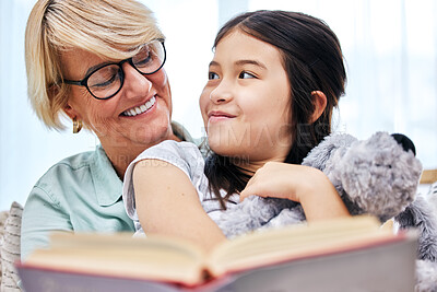 Buy stock photo Happy, book and senior woman with child reading for knowledge with teddy bear at home together. Smile, bonding and elderly grandmother relaxing and enjoying story with girl kid holding toy at house.