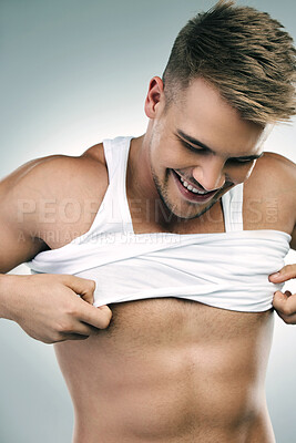 Buy stock photo Studio shot of a handsome young man taking his tank top off against a grey background