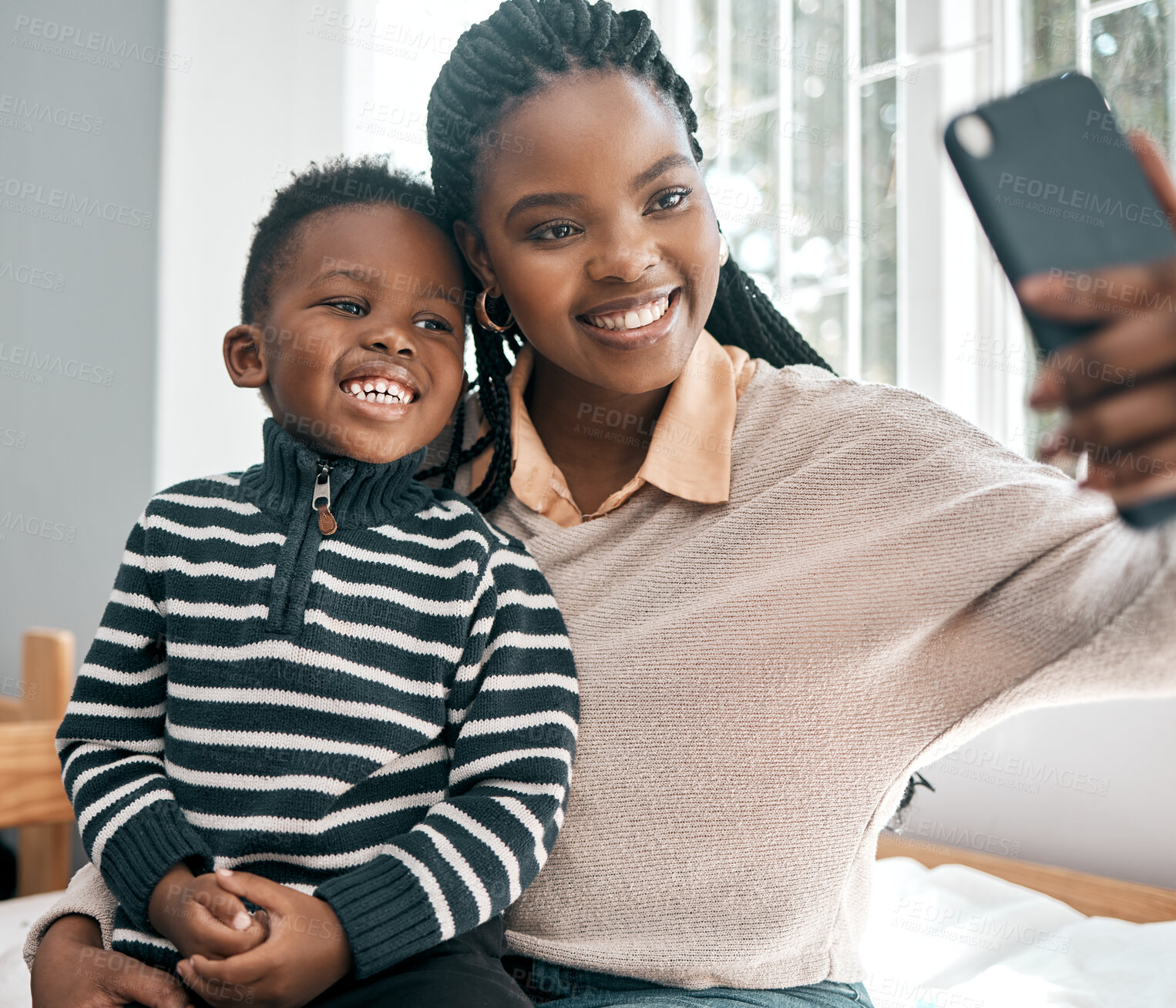 Buy stock photo Cropped shot of an attractive young woman and her adorable son taking selfies while sitting on a bed at home