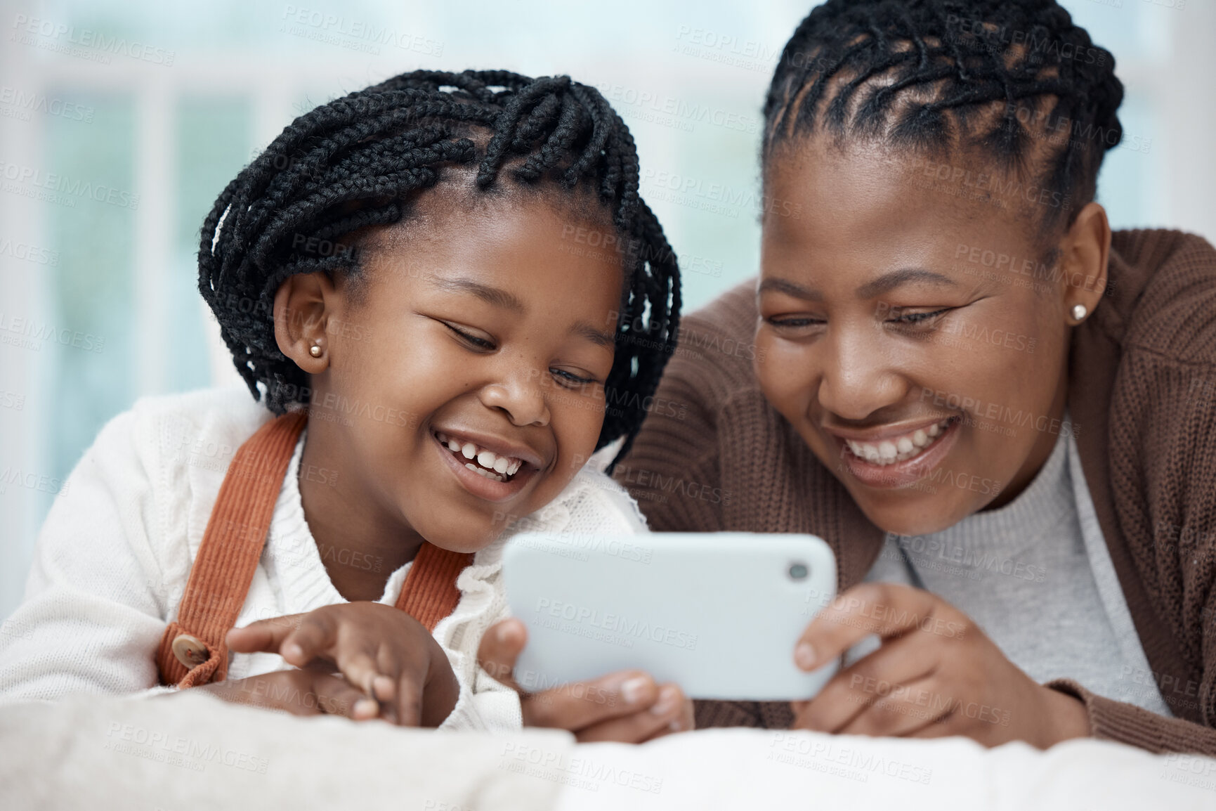 Buy stock photo Shot of a young mother lying on the bed with her daughter and bonding while using a cellphone