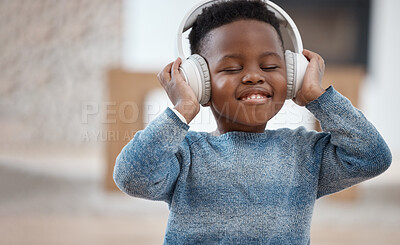 Buy stock photo Shot of an adorable little boy listening to music through headphones during a day at home