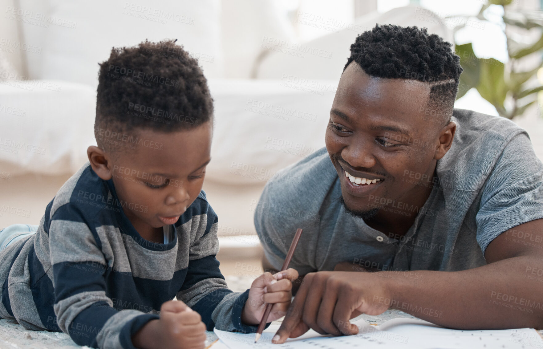 Buy stock photo Shot of a young father lying on the the living room floor and helping his son draw