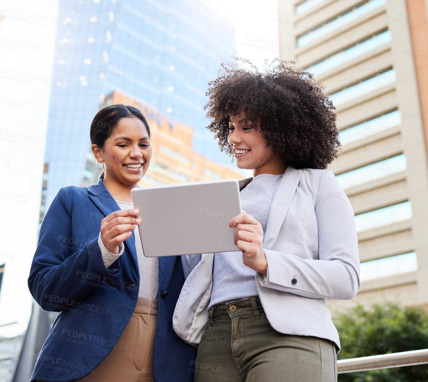 Buy stock photo Shot of two young businesswomen standing outside on the balcony and using a digital tablet