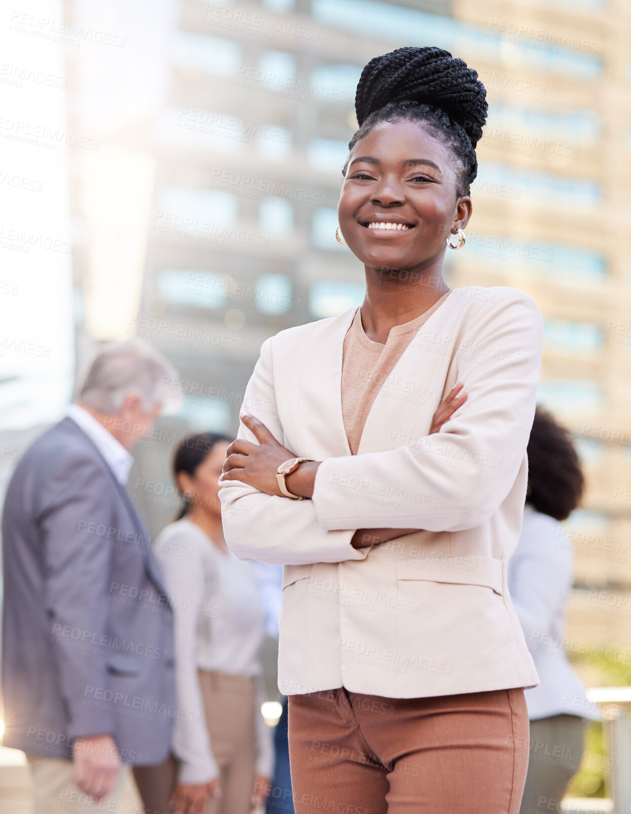 Buy stock photo Shot of an attractive young businesswoman standing outside with her arms folded while her colleagues discuss behind her