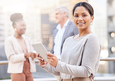 Buy stock photo Shot of an attractive young businesswoman standing outside and using a digital tablet while her colleagues discuss behind her