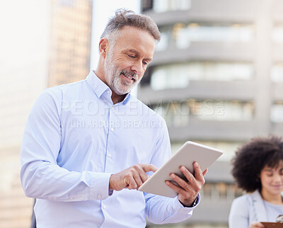 Buy stock photo Shot of a handsome mature businessman standing outside and using a digital tablet while his colleague stands behind him