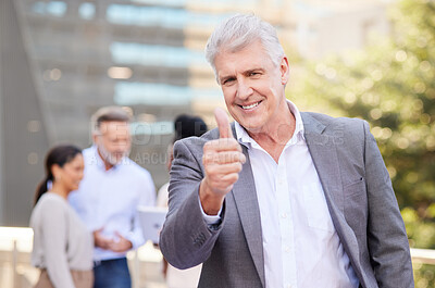 Buy stock photo Shot of a mature businessman standing outside and showing a thumbs up while his colleagues discuss behind him