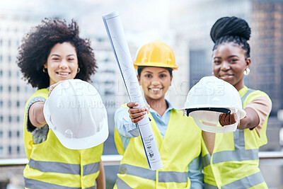 Buy stock photo Portrait of a group of confident young businesswomen holding blueprints and hardhats while working at a construction site