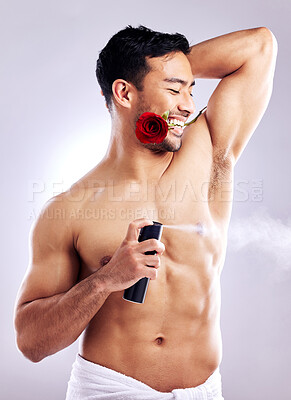 Buy stock photo Studio shot of a man spraying deodorant while posing with a rose in his mouth