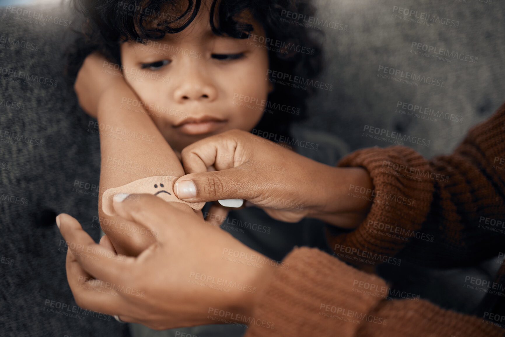 Buy stock photo Shot of a woman putting a plaster with a sad face drawn on it on her son's elbow