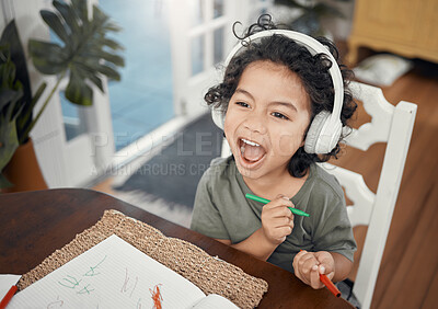 Buy stock photo Shot of an adorable little boy wearing headphones while drawing at home