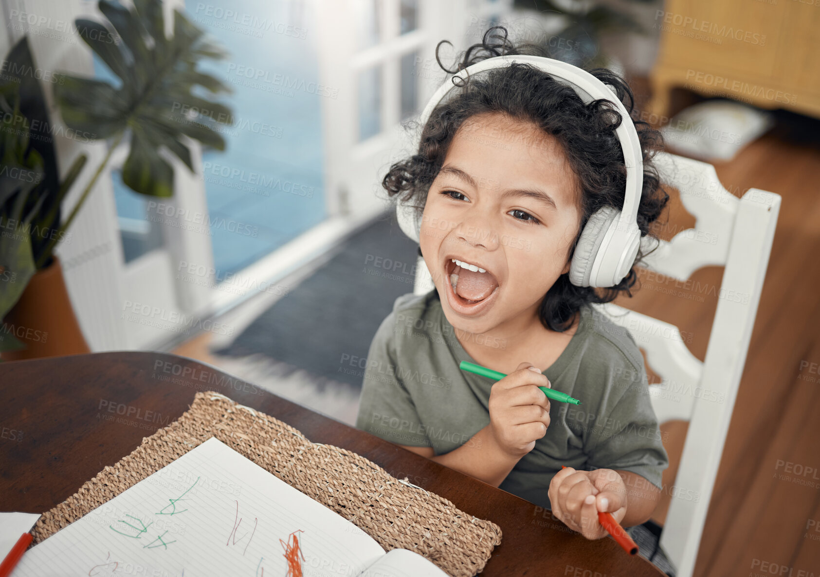 Buy stock photo Shot of an adorable little boy wearing headphones while drawing at home