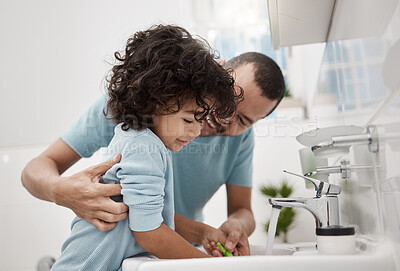 Buy stock photo Shot of a father helping his son rinse his toothbrush while brushing his teeth in the bathroom at home