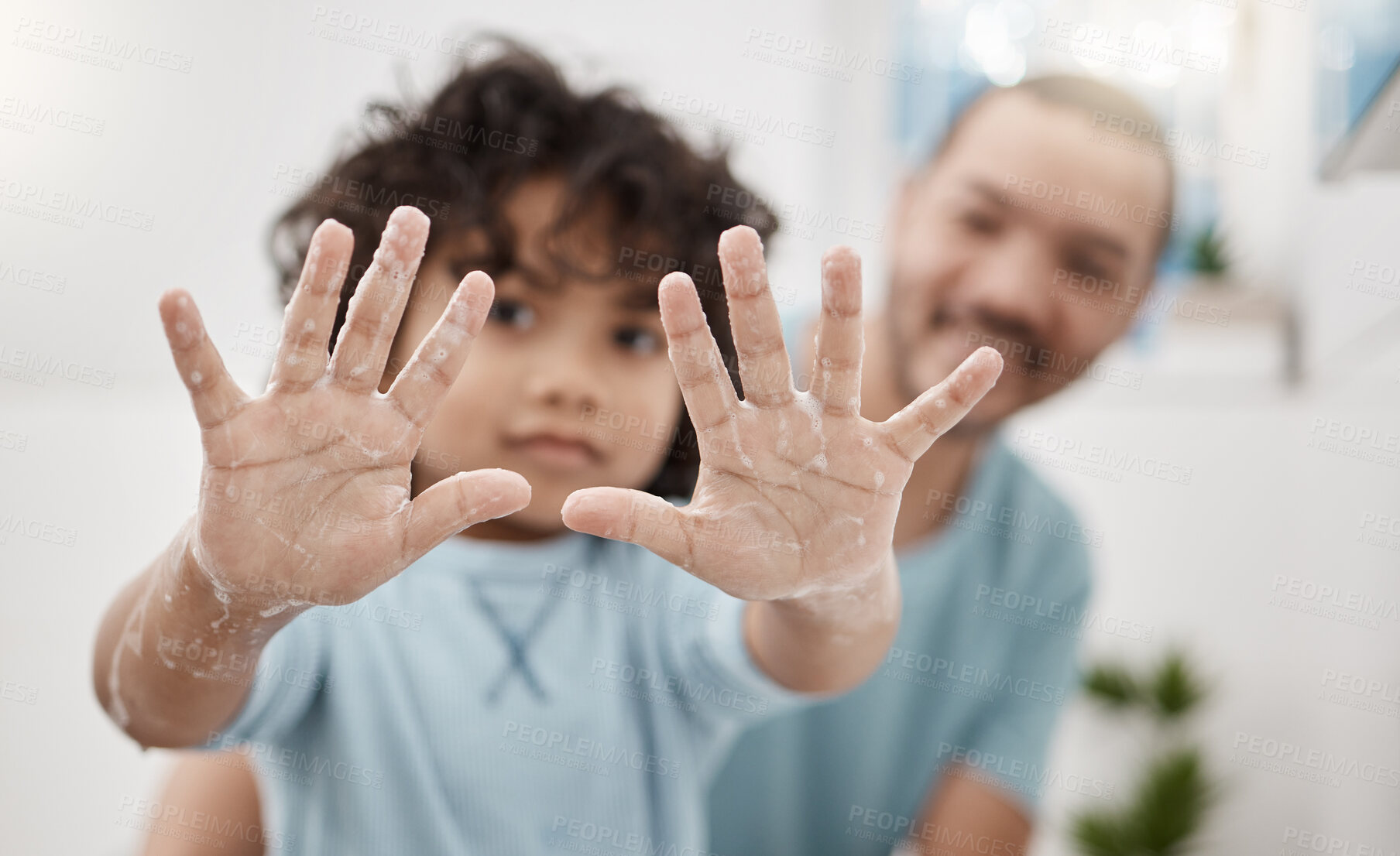 Buy stock photo Portrait of a little boy holding up his soapy hands while standing in a bathroom with his father at home