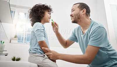 Buy stock photo Shot of a father brushing his little son's teeth in the bathroom at home