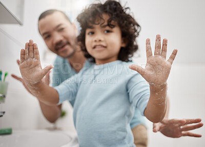 Buy stock photo Portrait of a little boy holding up his soapy hands while standing in a bathroom with his father at home