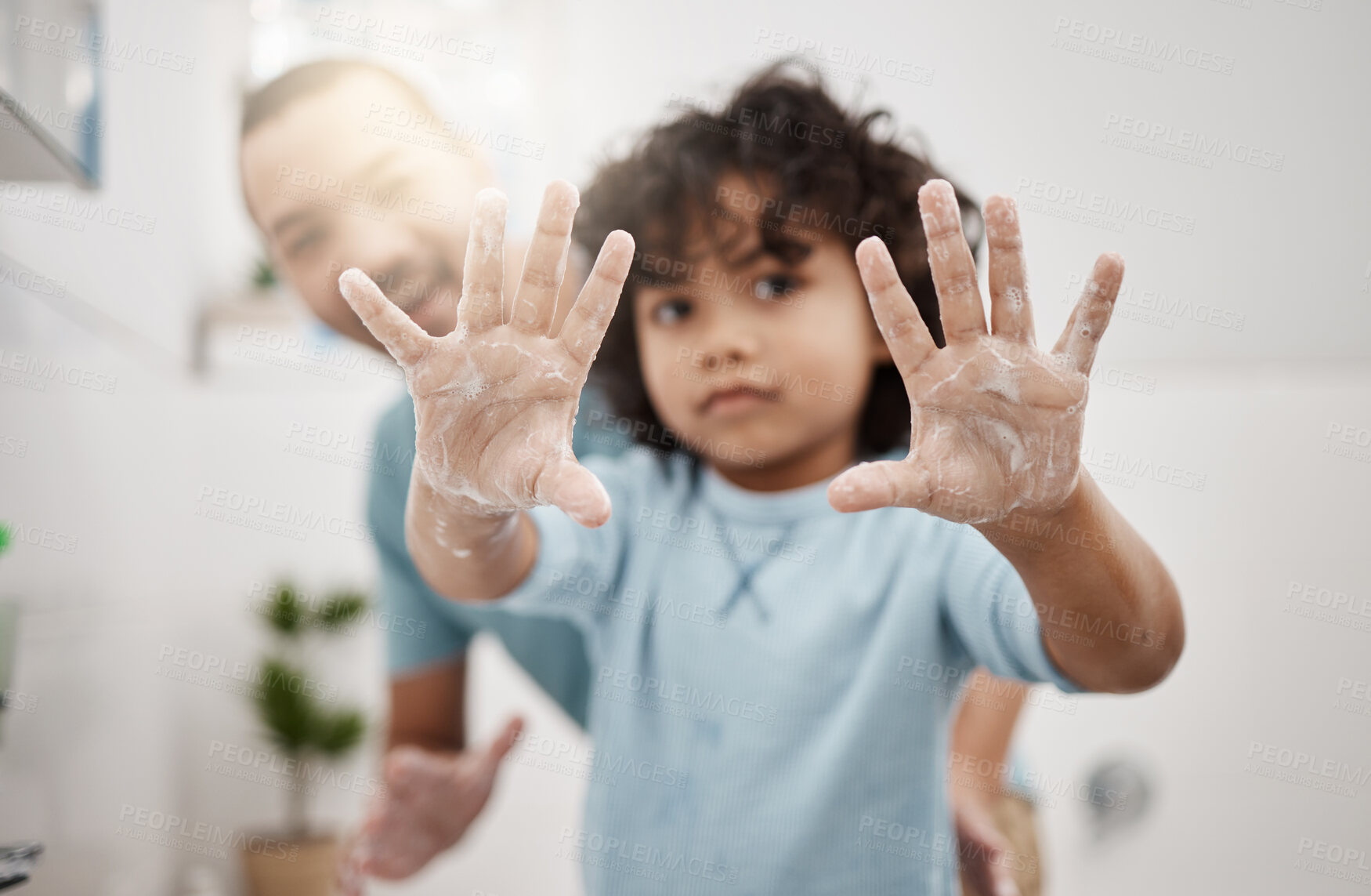 Buy stock photo Portrait of a little boy holding up his soapy hands while standing in a bathroom with his father at home