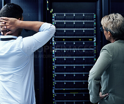 Buy stock photo Rearview shot of two technicians looking stressed while working in a data centre