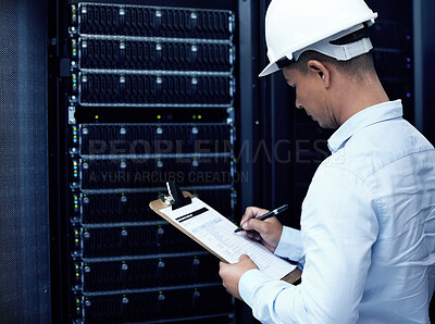 Buy stock photo Shot of a young man making notes while working in a server room