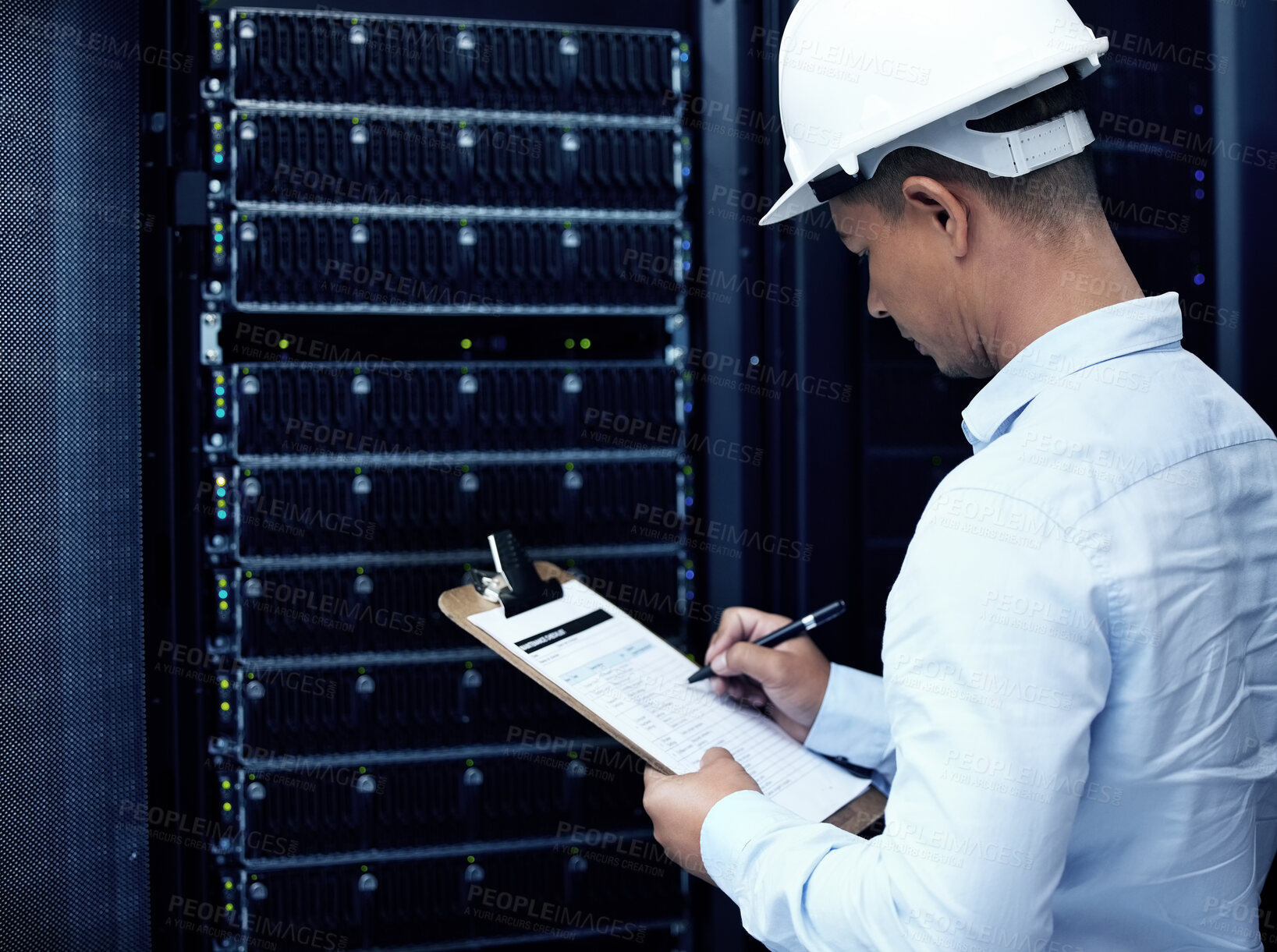 Buy stock photo Shot of a young man making notes while working in a server room